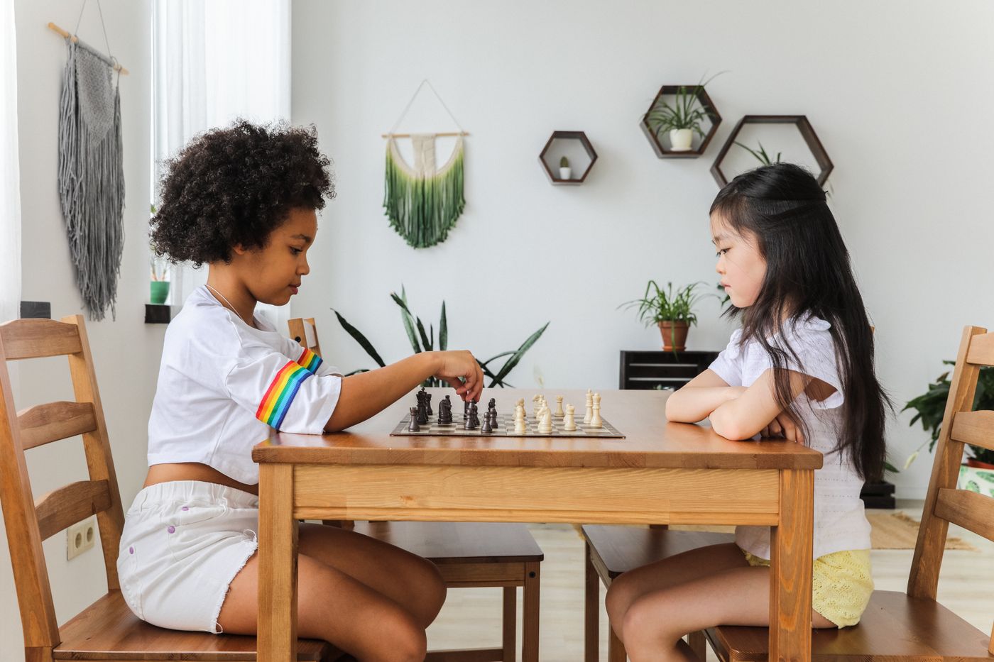 Dos niñas juegan una partida de ajedrez frente a frente en una mesa de madera